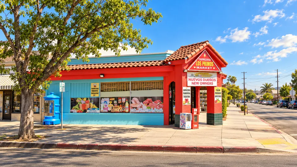 Los Primos Market's red and blue corner storefront with its tiled-roof sign on East Alisal Street in warm daylight