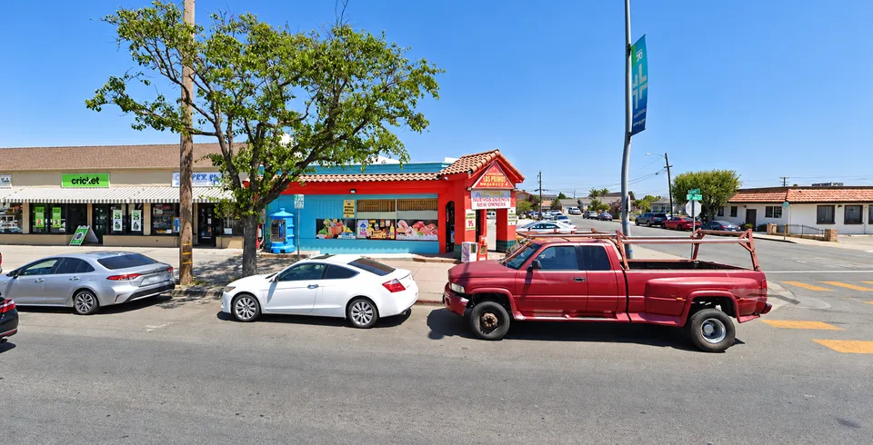 Street view of Los Primos Market's red and blue storefront on East Alisal Street with cars parked out front